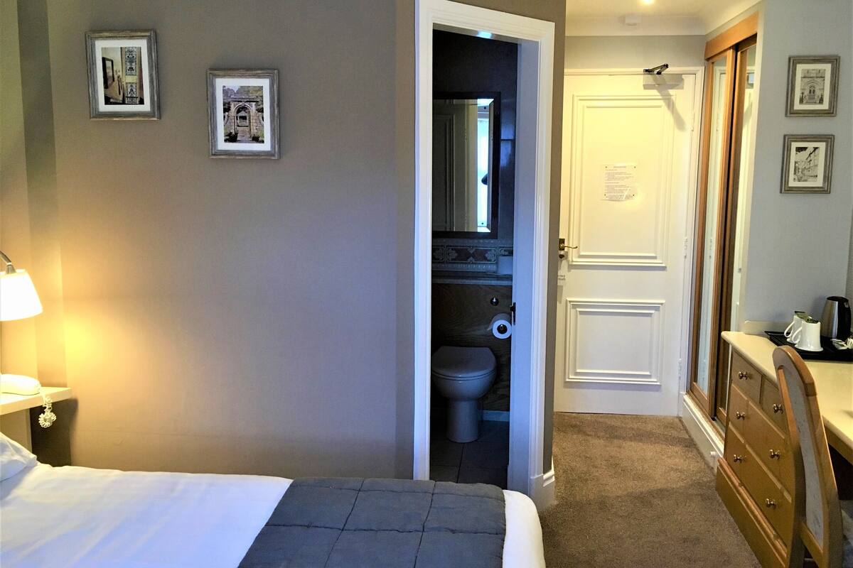 A hotel room with a bed, a desk, a dresser, and a bathroom visible through an open door.
