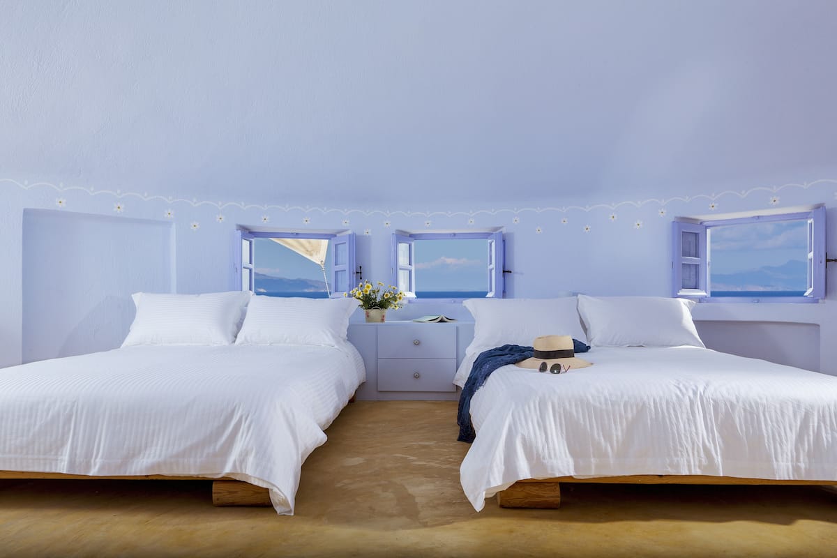A room with two beds, a nightstand, and a view of the sea through windows.