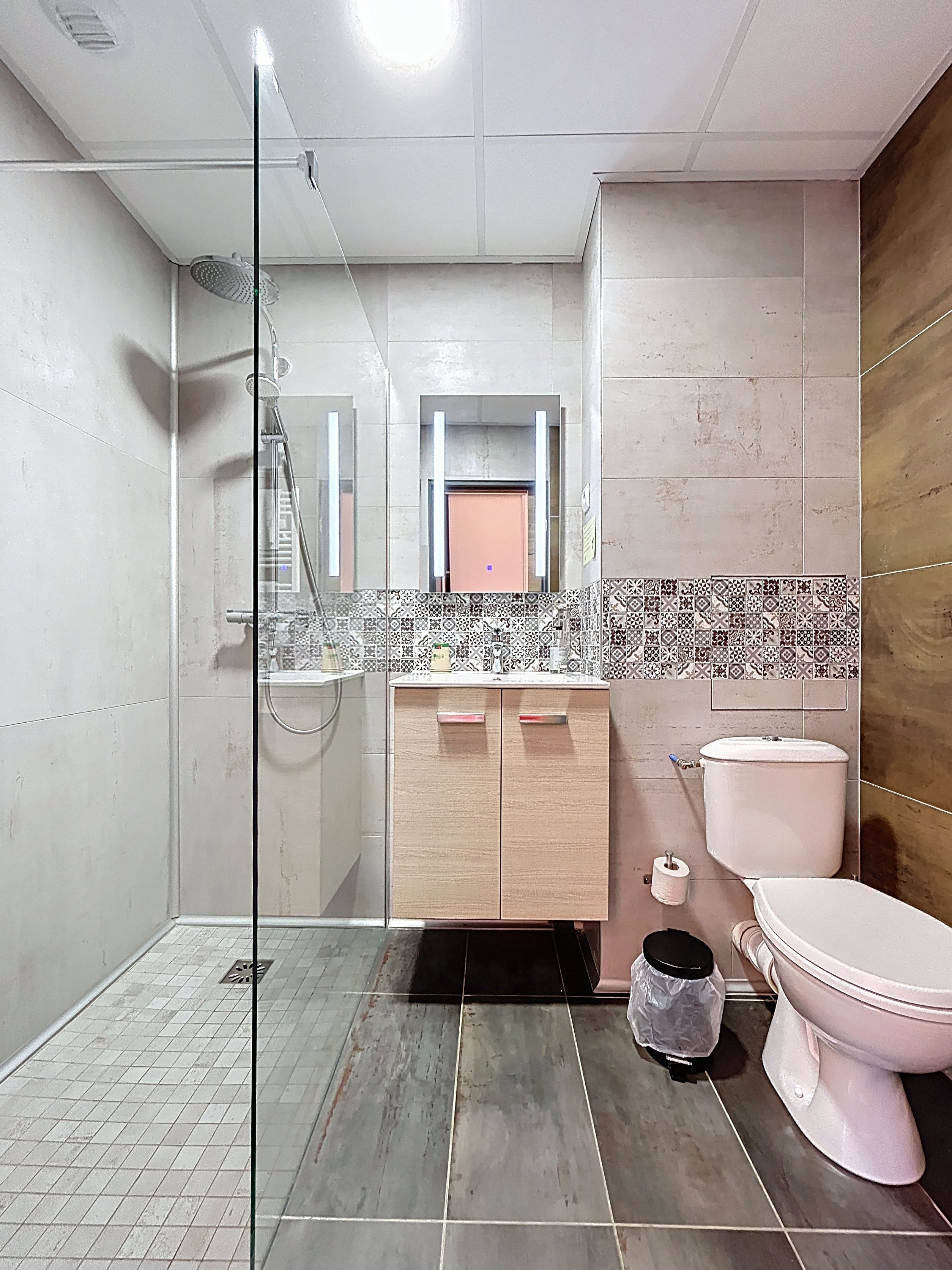 A bathroom with a glass shower enclosure, a wooden vanity with a mirror, a toilet, and a sink.