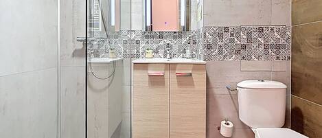 A bathroom with a glass shower enclosure, a wooden vanity with a mirror, a toilet, and a sink.