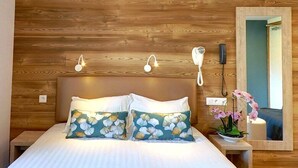 Un dormitorio con cabecera de madera, dos lámparas de noche, un teléfono junto a la cama, un espejo y una almohada con estampado floral.