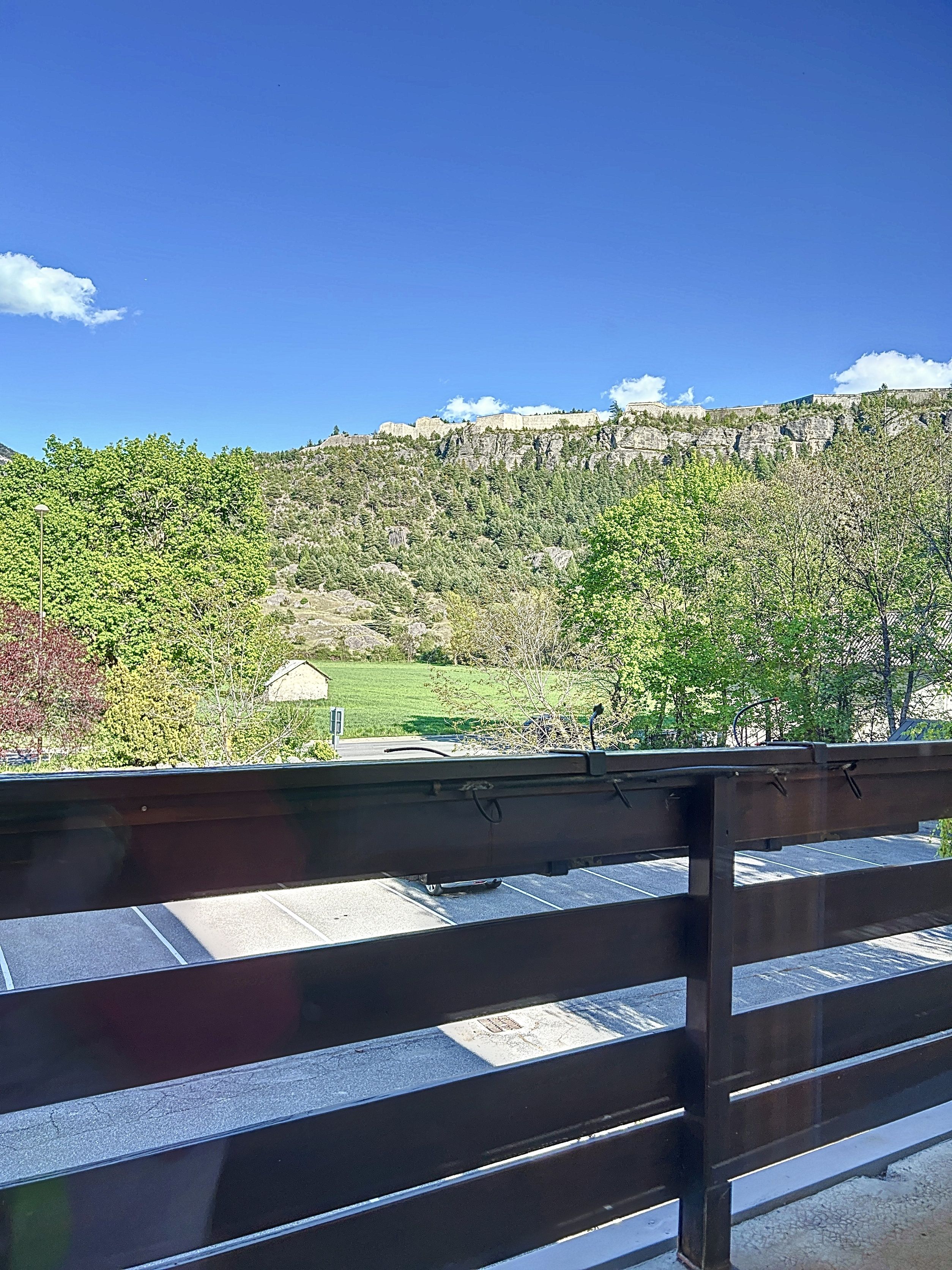 A view from a balcony with a railing, overlooking a mountainous landscape with trees and a clear sky.