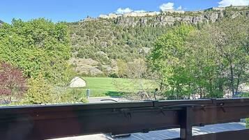 Vista desde un balcón con barandilla, que da a un paisaje montañoso con árboles y cielo despejado.