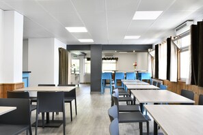 A modern dining area with rectangular tables and chairs, a kitchen in the background, and large windows with curtains. - Hotel Lacour (Eygliers)
