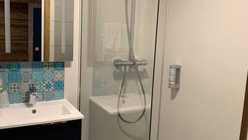 A modern bathroom with a glass-enclosed shower, a white sink, and a tiled backsplash.