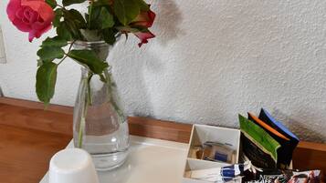 A table with a vase of roses, a white mug, and a card holder with books and a pen.