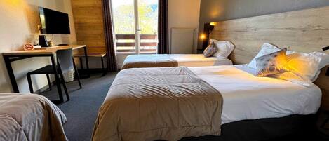 A hotel room with two beds, a desk, a television, and a view of the outdoors.