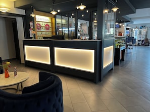 A reception area with a modern design, featuring a reception desk with illuminated panels, a seating area with a round table and chairs, and a visible bar area in the background. - Hotel Lacour (Eygliers)