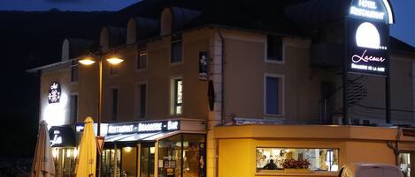 A hotel with a restaurant and bar, a parking area, and a mountain backdrop.