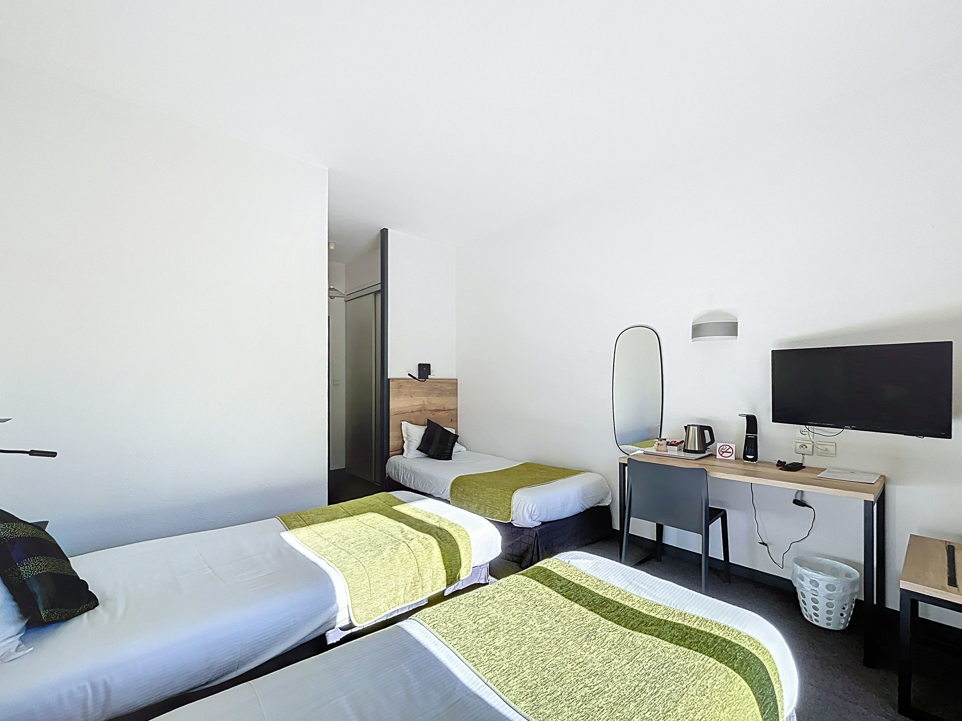 A hotel room with two single beds, a desk with a computer, a flat-screen TV, and a mirror.
