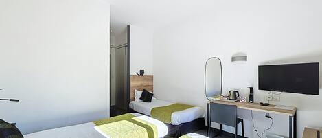 A hotel room with two single beds, a desk with a computer, a flat-screen TV, and a mirror.