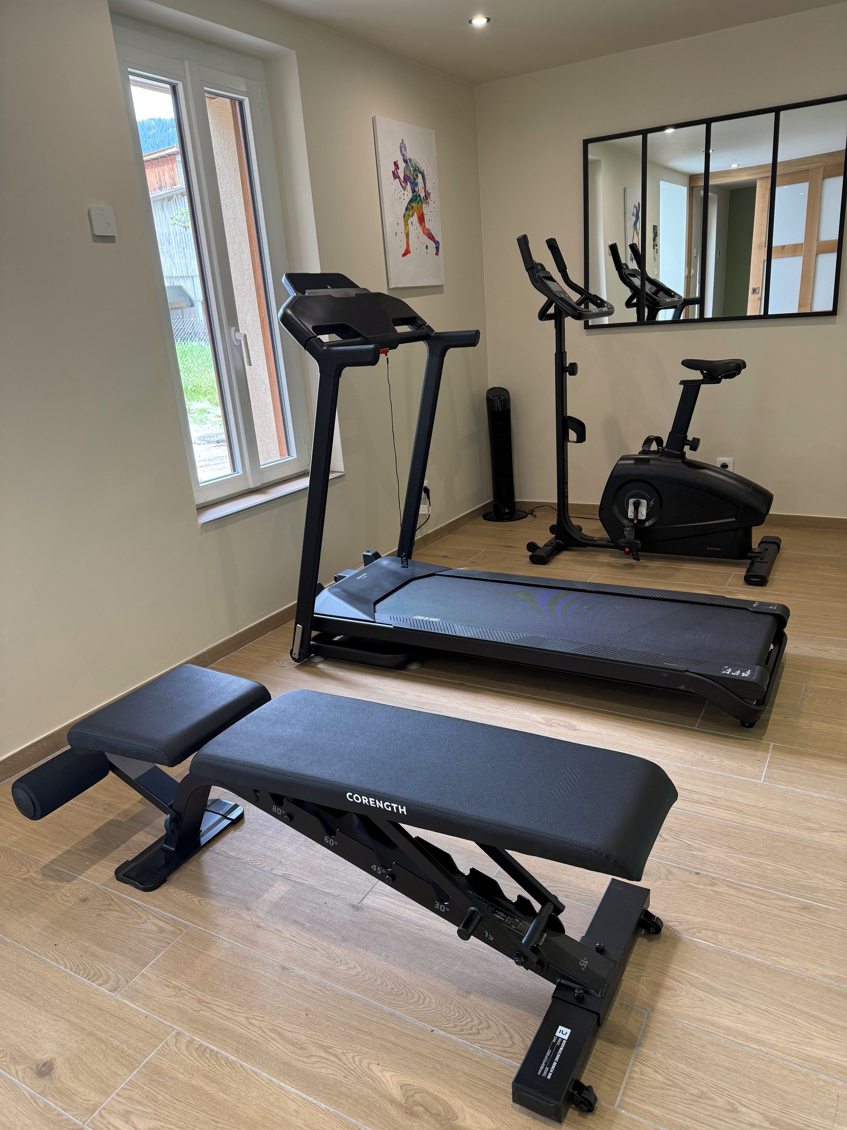 Een huisgym met een loopband, elliptische trainer en gewichtbank.