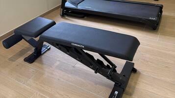 Een huisgym met een loopband, elliptische trainer en gewichtbank.