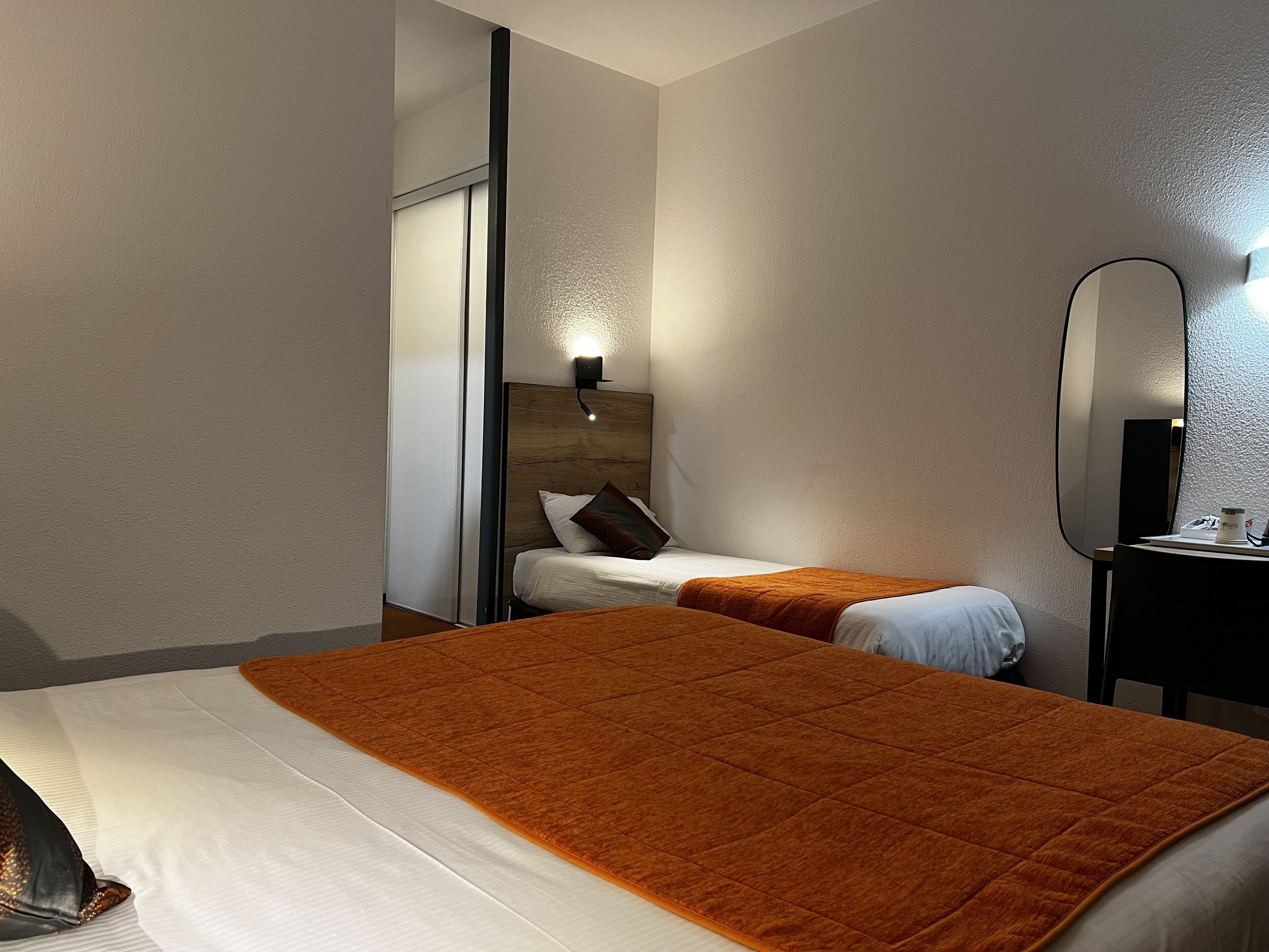 A hotel room with a large bed, a smaller bed, a mirror, and a nightstand.