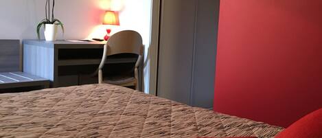 A hotel room with a bed, a desk, a chair, and a lamp.