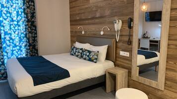 A modern hotel room with a wooden headboard, a large mirror, a bedside table, and a small stool.