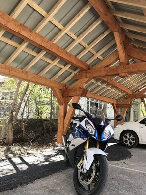A motorcycle parked under a wooden structure with a corrugated metal roof. - Hotel Lacour (Eygliers)