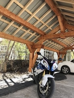 Una motocicleta estacionada bajo una estructura de madera con techo de lámina corrugada.