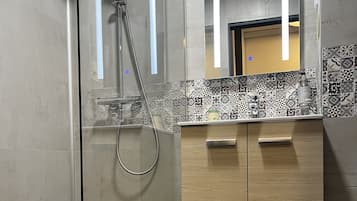 Un baño moderno con ducha envuelta en vidrio, tocador de madera con espejo y baldosas estampadas en la pared.
