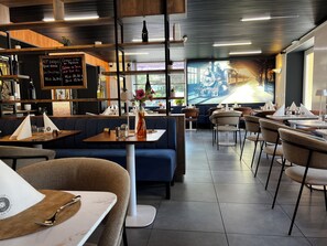 Un interior de restaurante moderno con estantes de madera, un menú en pizarra y un gran ventanal con vista a un tren.