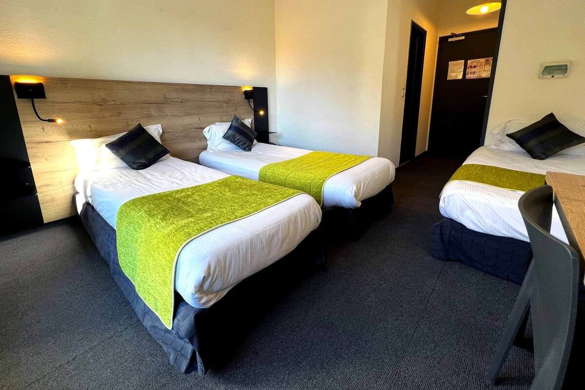 Een hotelkamer met twee bedden, elk voorzien van een groene plaid, een houten hoofdbord en een nachtkastje met een lamp.