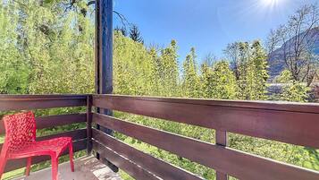 Un balcon en bois avec une chaise en plastique rouge, donnant sur un paysage montagneux parsemé d’arbres verdoyants.
