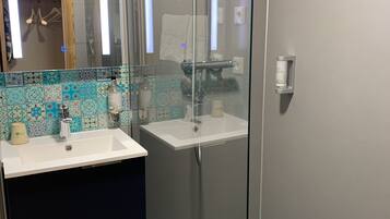 A modern bathroom with a glass shower enclosure, a white sink, and a tiled backsplash.