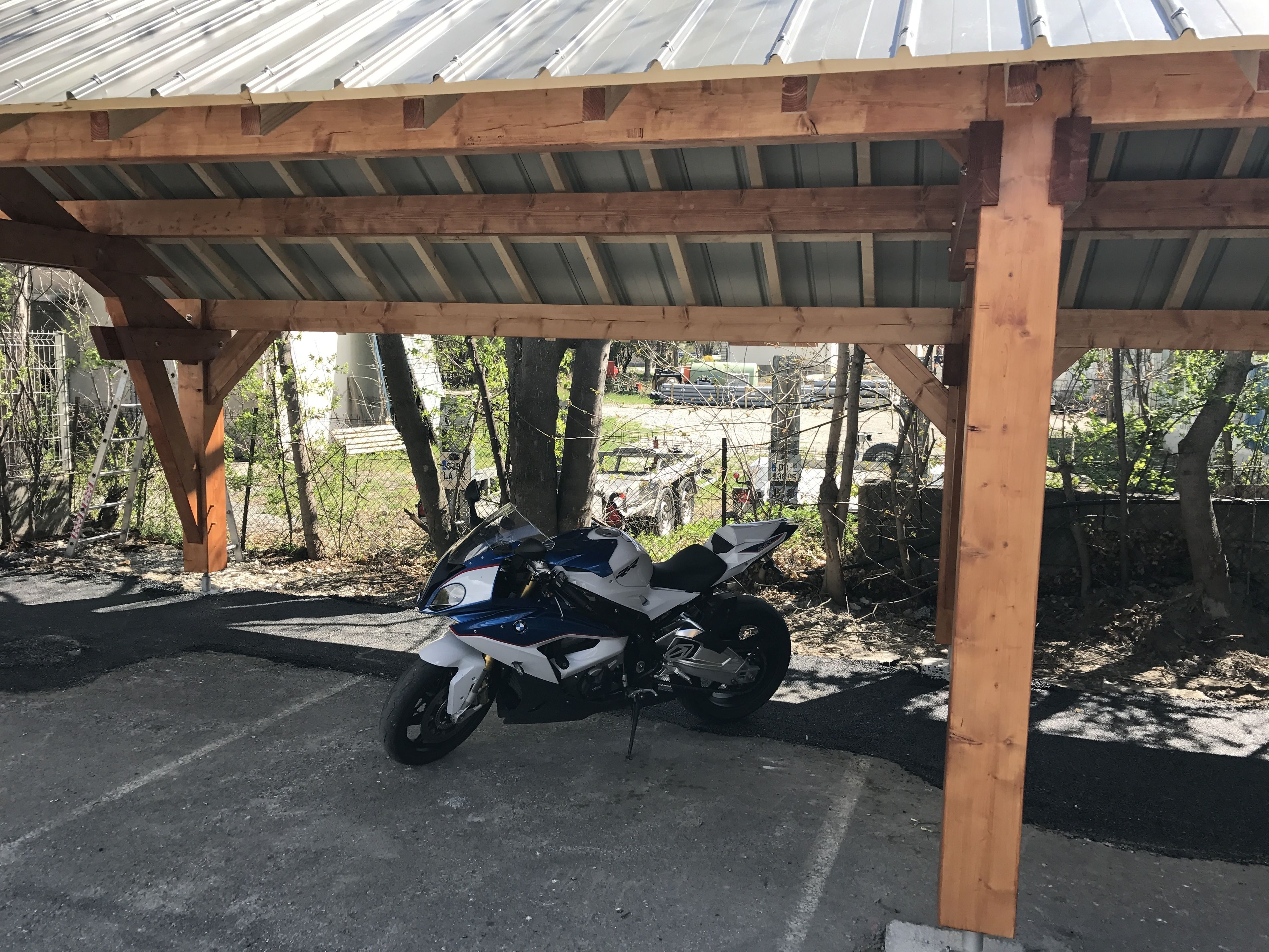 A motorcycle parked under a wooden shelter with a metal roof.