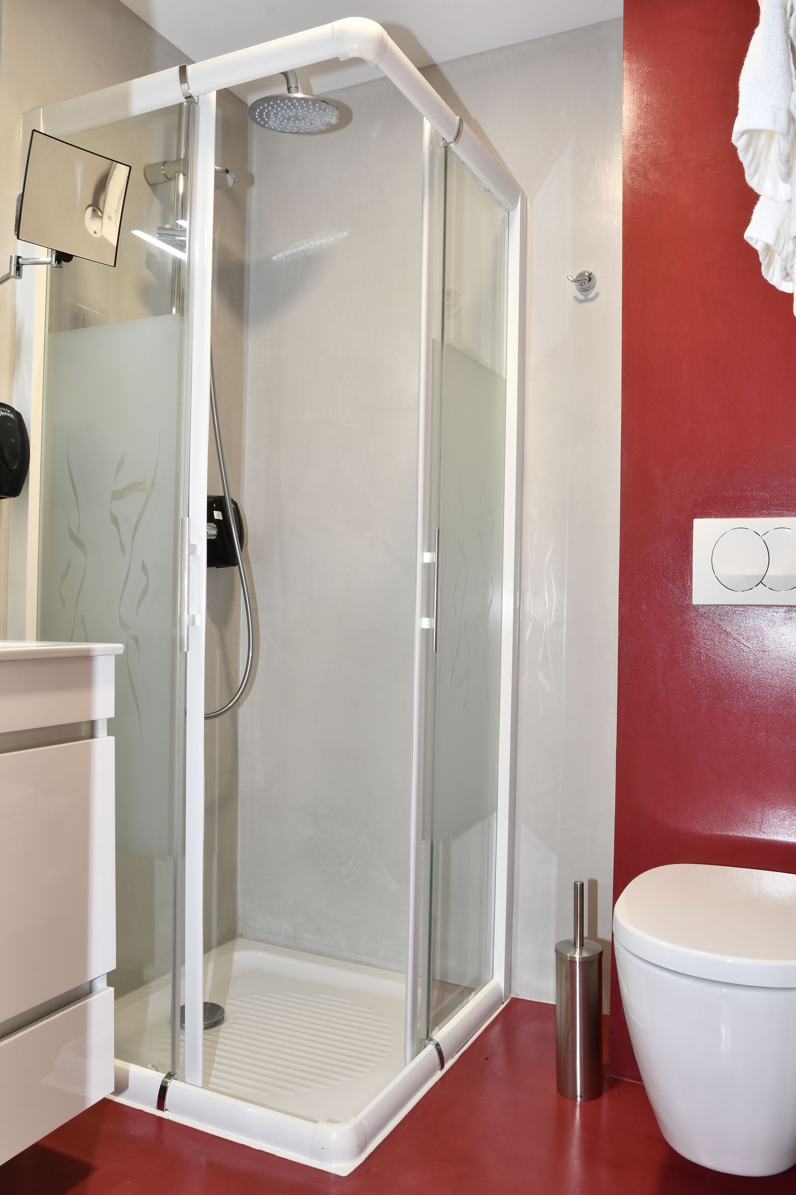 Une salle de bain moderne avec une douche à parois de verre, des toilettes blanches et un mur d’accent rouge.