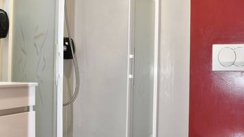 A modern bathroom with a glass-enclosed shower, a white toilet, and a red accent wall.