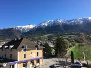 A building with a sloped roof and a solar panel on the roof, located in a valley with a mountain range in the background. - Hotel Lacour (Eygliers)
