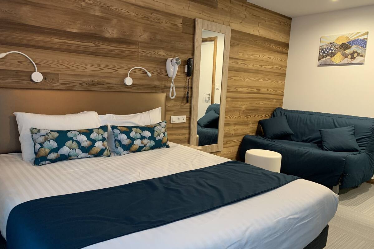 Een slaapkamer met een groot bed, een nachtkastje, een stoel, een spiegel en een telefoon aan de muur.