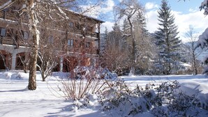 Un edificio cubierto de nieve con múltiples ventanas y un balcón, rodeado de árboles y nieve.