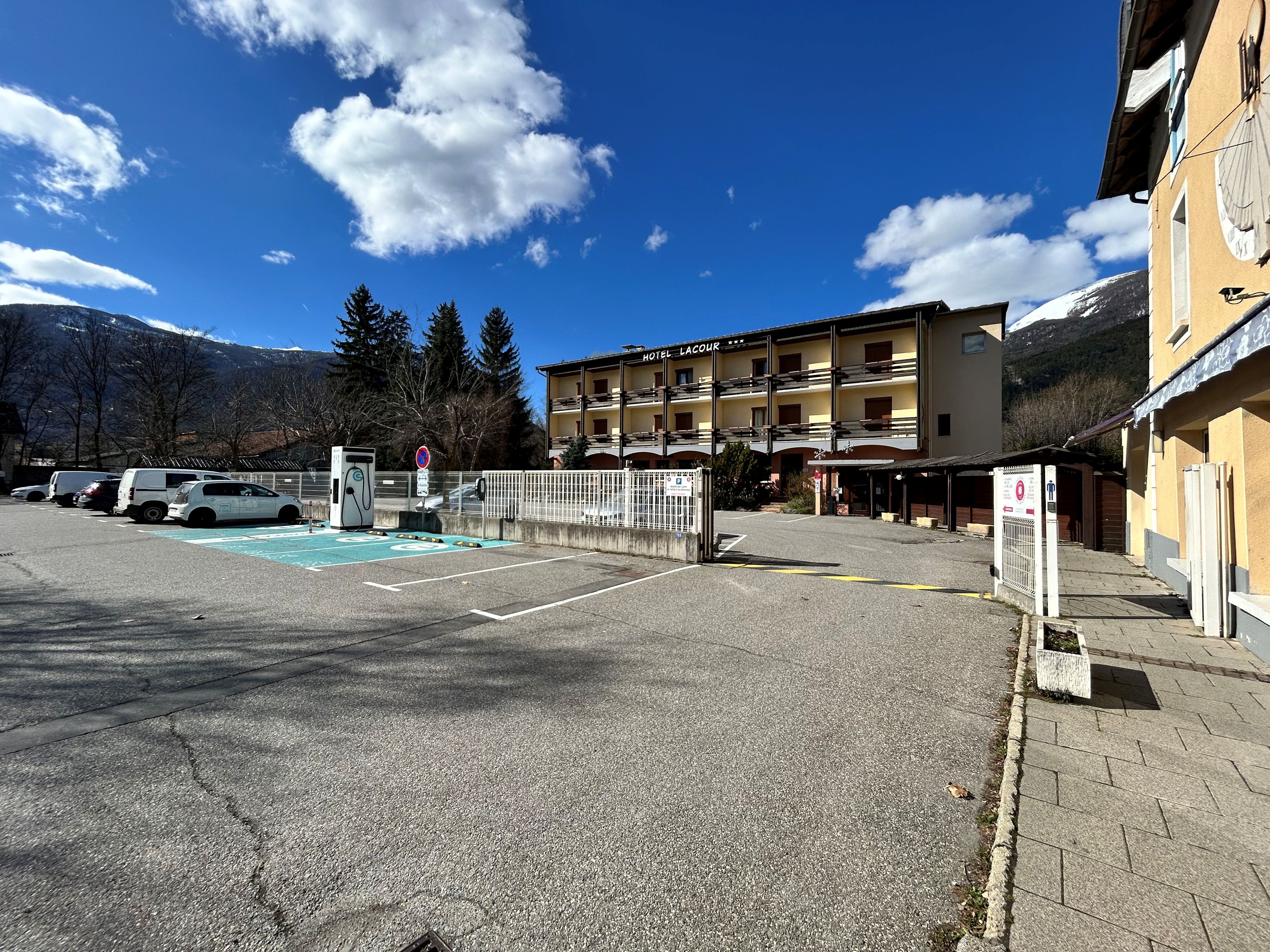 Un hotel con estacionamiento, un cartel que dice 'HOTEL LACOUR' y una montaña al fondo.