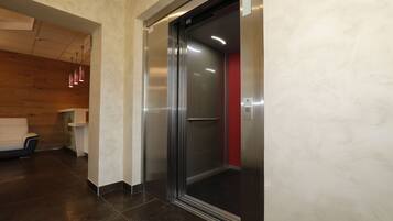 Un ascenseur dans un immeuble moderne, avec une finition métallique et un intérieur rouge.
