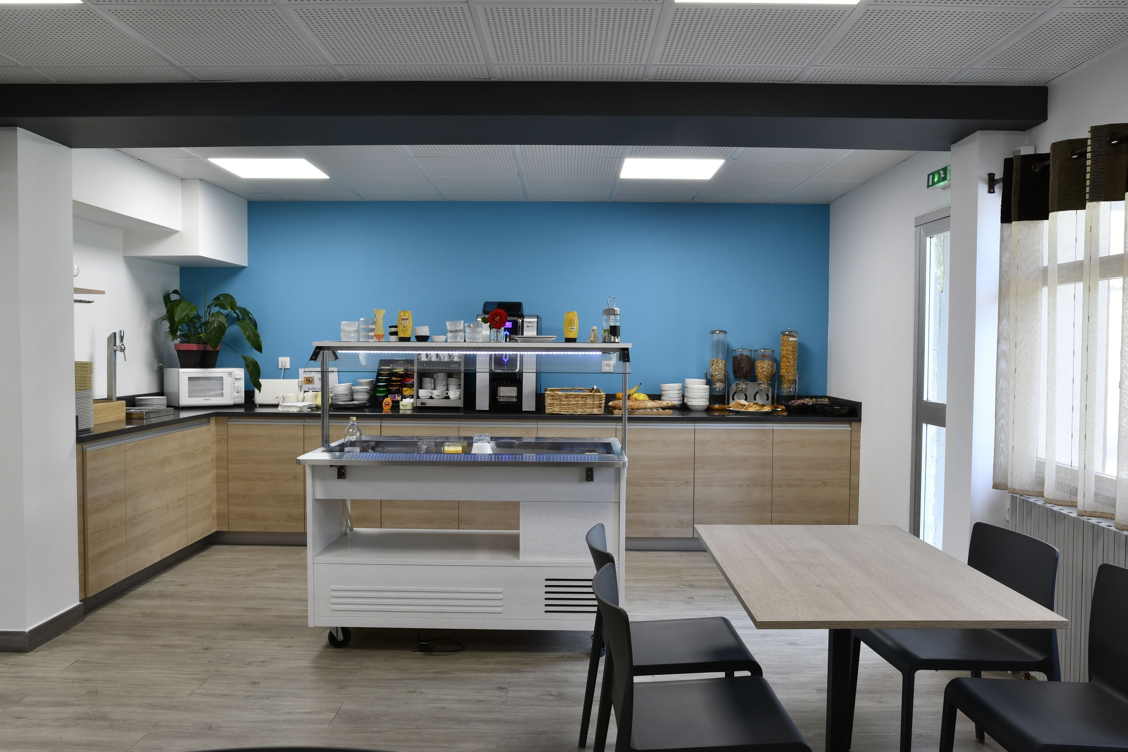 A modern kitchen with a blue accent wall, a coffee machine, and a buffet counter.