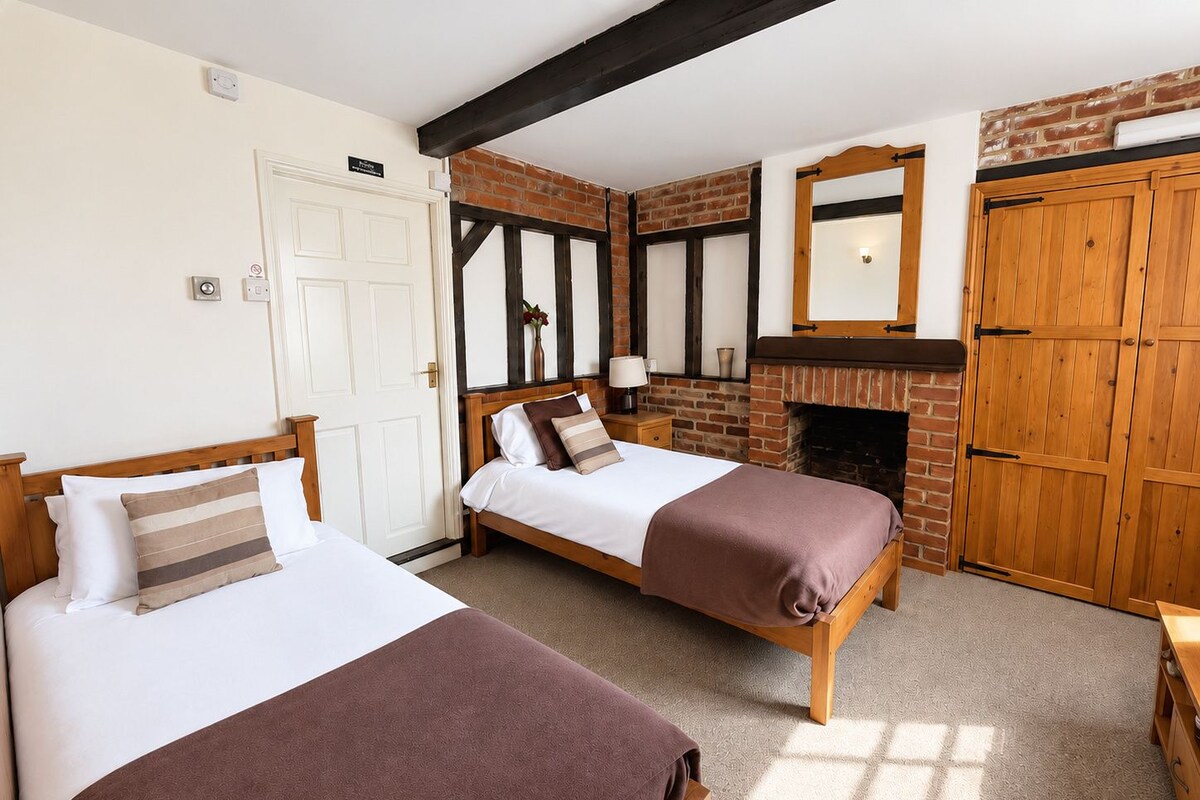 A room with two beds, a brick fireplace, and wooden wardrobes.