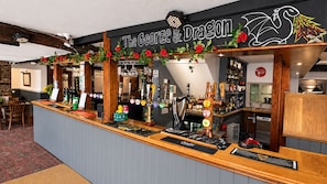 A bar area with a sign reading 'The George & Dragon,' featuring a wooden counter, multiple taps, and a variety of bottles. - The George and Dragon Hotel (Sudbury)