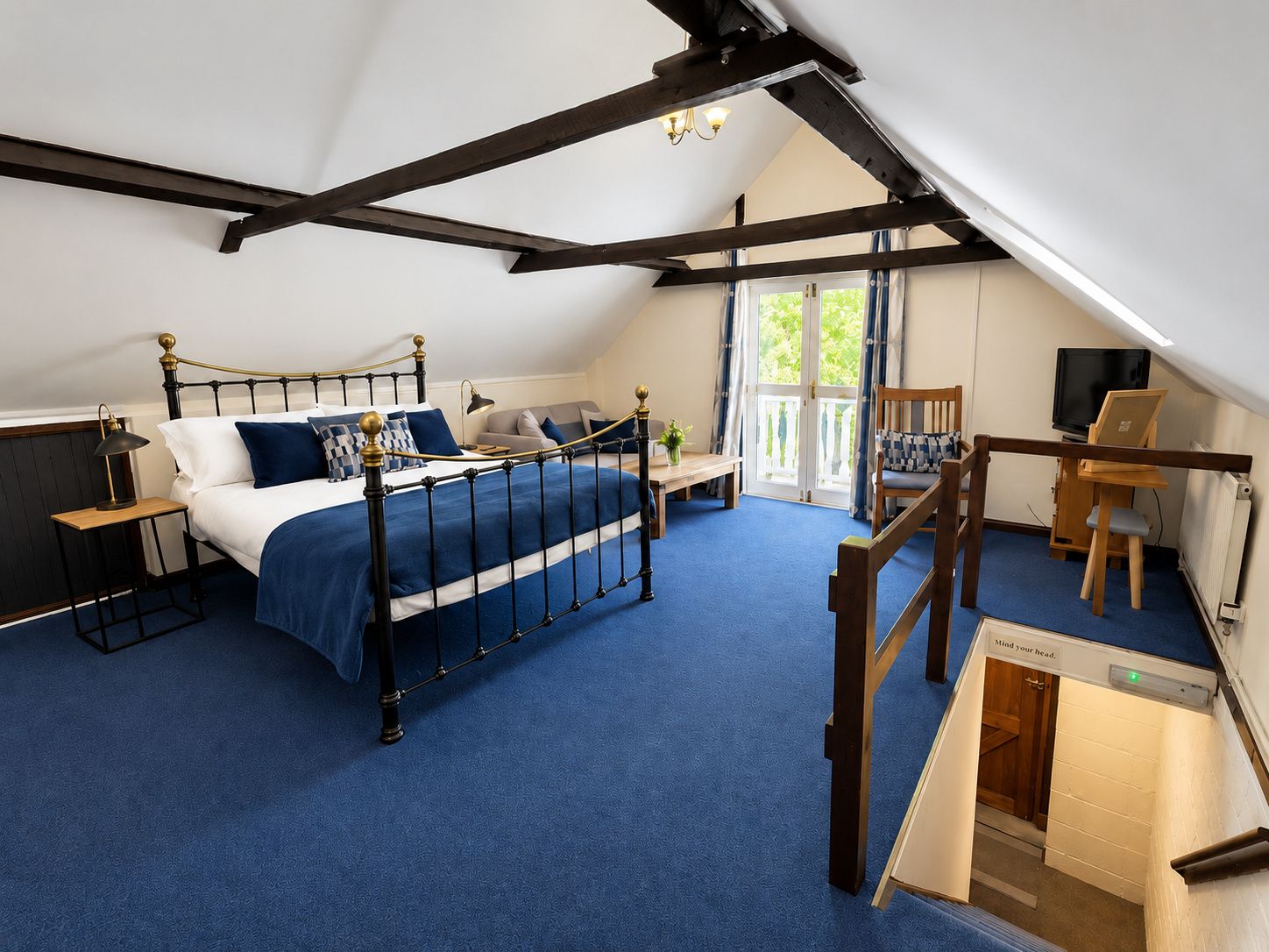 A bedroom with a bed, a desk, a chair, a television, and a balcony.