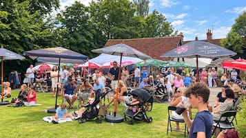 An outdoor gathering with people seated under umbrellas, some with children.