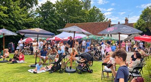 An outdoor gathering with people seated under umbrellas, some with children.