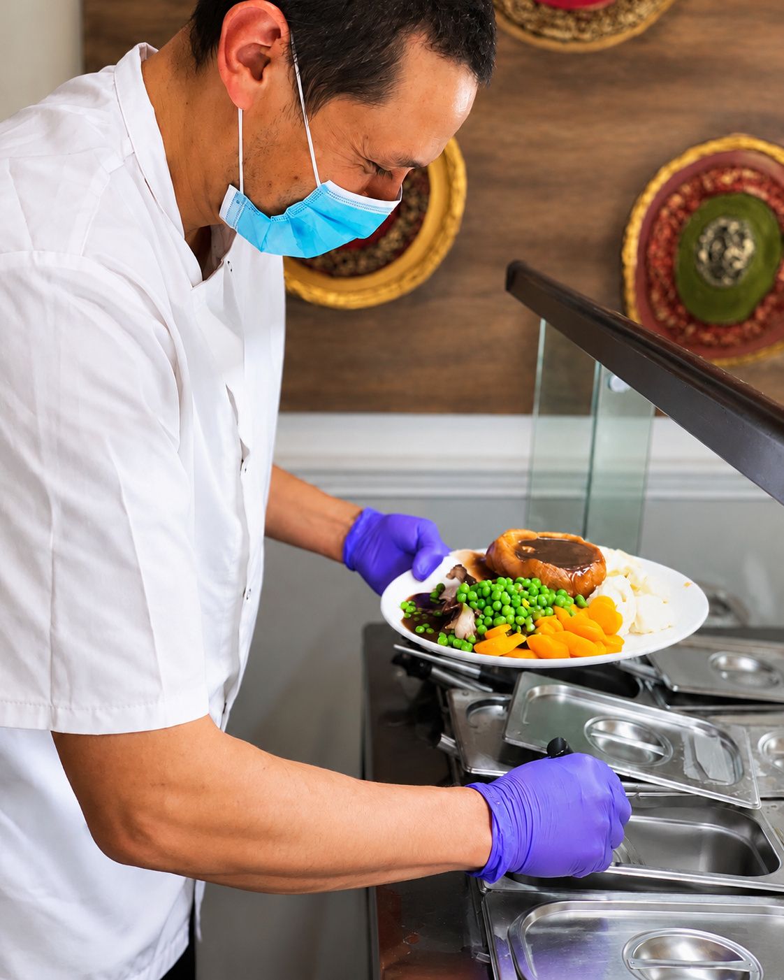 A person in a white uniform and purple gloves serving food on a plate.