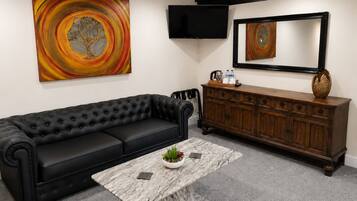 A living room with a black leather sofa, a marble coffee table, a wooden cabinet, and two abstract paintings.