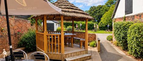 An outdoor patio area with a wooden gazebo, tables, and chairs.