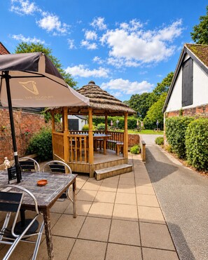 An outdoor patio area with a wooden gazebo, tables, and chairs. - The George and Dragon Hotel (Sudbury)