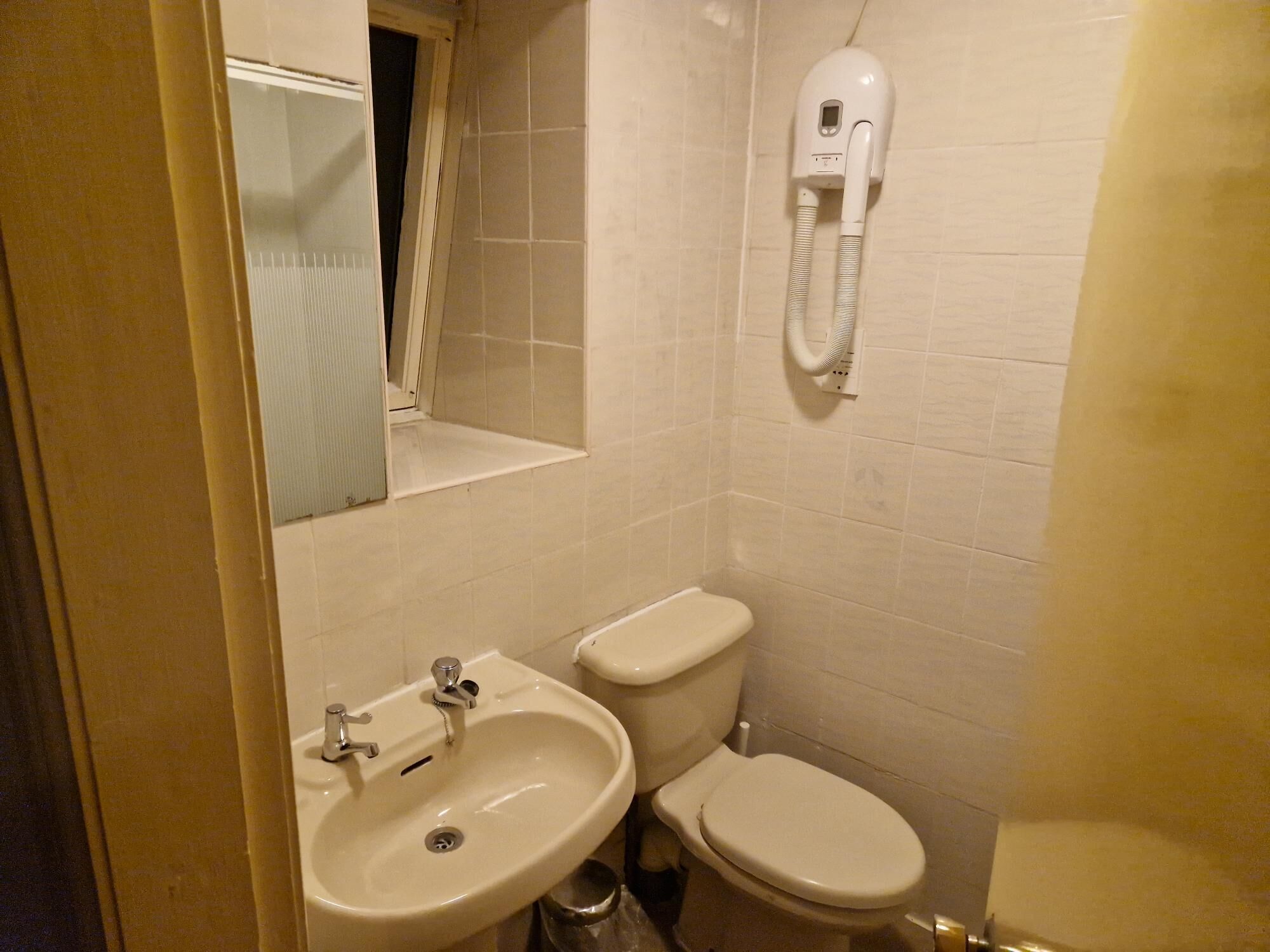 A small bathroom with a sink, toilet, and a hairdryer mounted on the wall.