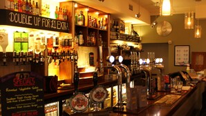 A bar with multiple taps, shelves of bottles, and a menu board. - The Menai Hotel and Bar (Bangor)