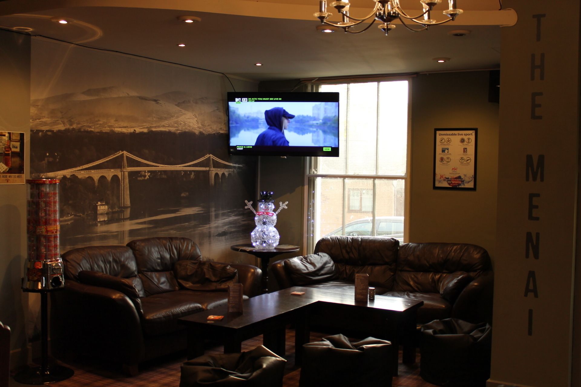 A living room with leather sofas, a coffee table, a TV mounted on the wall, and a large window.