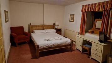 A bedroom with a wooden bed, a red armchair, a desk with a mirror, and a radiator.