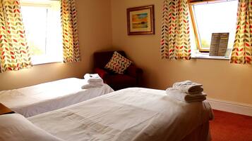 A hotel room with two single beds, a red armchair, and a window with a view of the countryside.